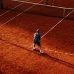Tennis players competing on a sunlit red clay court in Buenos Aires.